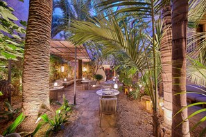An outdoor patio area with stone flooring, round tables, wicker chairs, and ambient lighting. - Palacio Can Marqués (Palma de Mallorca)