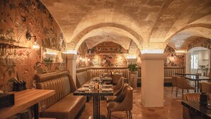A restaurant with a long communal table, cushioned seating, and a stone ceiling. - Palacio Can Marqués (Palma de Mallorca)