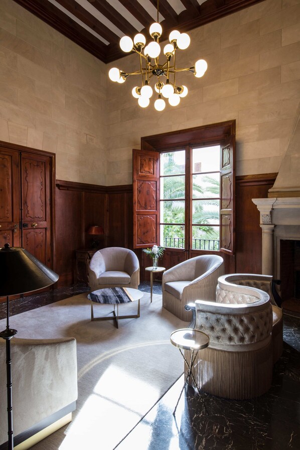 A spacious room with a high ceiling, wooden paneling, a large chandelier, and a view of palm trees through a window. - Palacio Can Marqués (Palma de Mallorca)