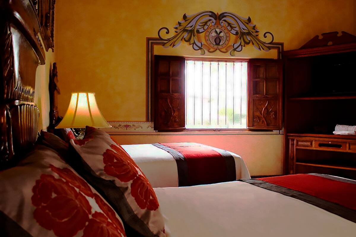 Een hotelkamer met twee bedden, een raam met tralies, een houten hoofdbord, een lamp en een televisie op een houten standaard.