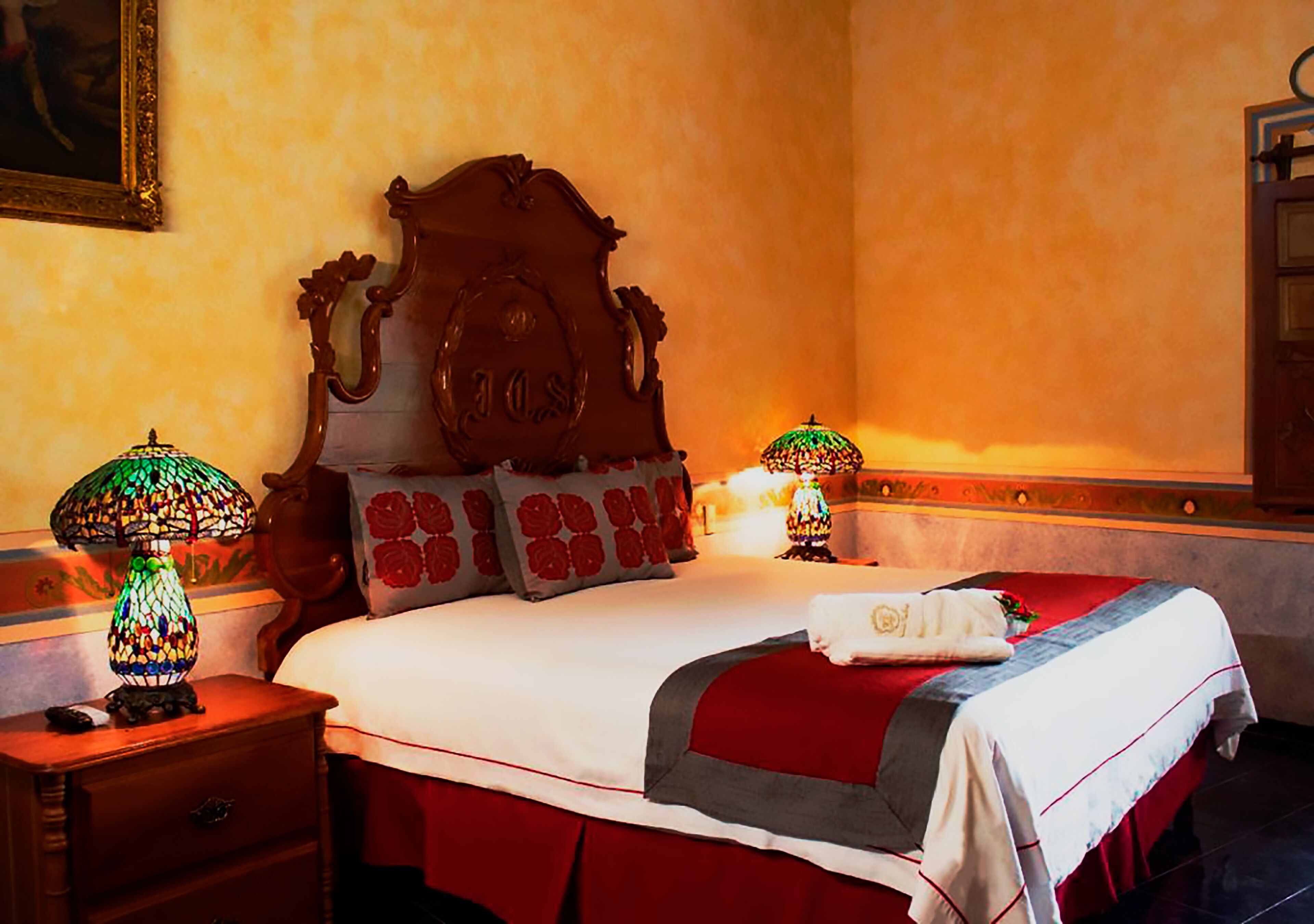 Una habitación de hotel con una cama grande, dos mesitas de noche, un cabecero de madera y dos lámparas decorativas.