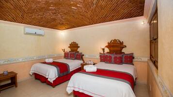 Quarto de hotel com duas camas, cabeceira de madeira, mesa de cabeceira pequena e teto de tijolos.