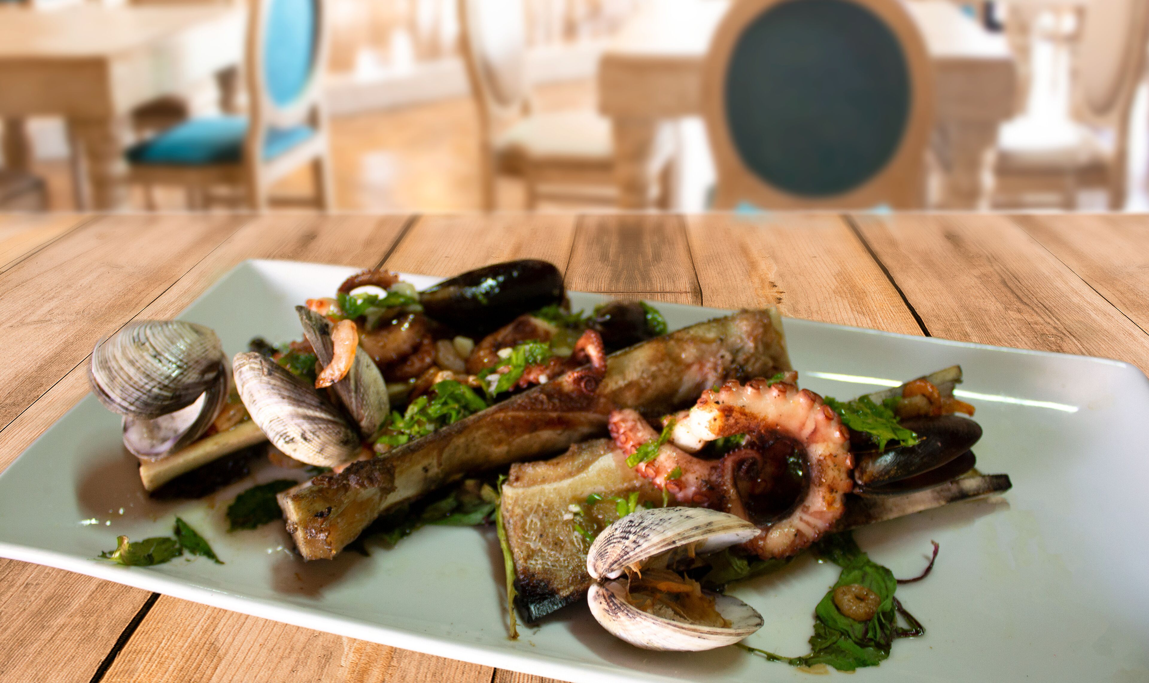 A seafood dish on a white plate with clams, mussels, and a piece of fish, served on a wooden table.