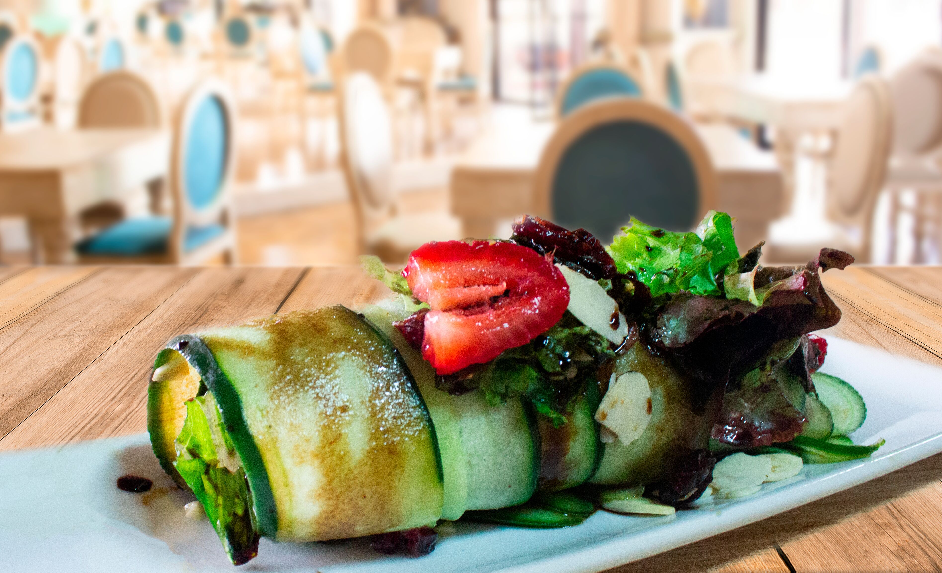 Un plato de comida con un wrap, ensalada y una rodaja de tomate sobre una mesa de madera en un restaurante.