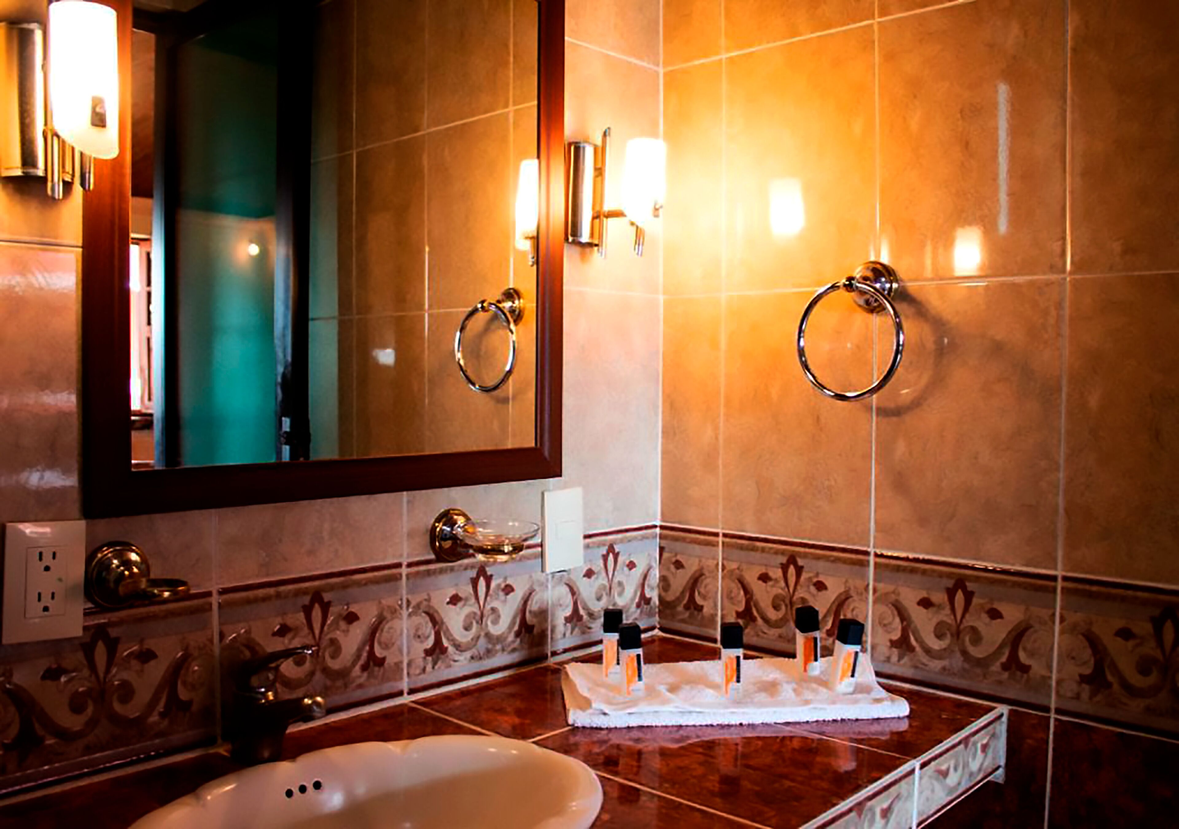 A bathroom with a large mirror, two towel rings, a sink, and decorative wall tiles.