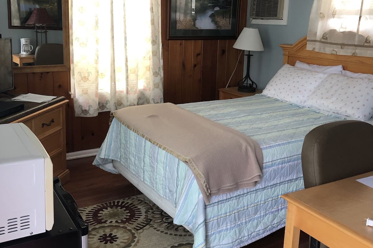 Een slaapkamer met een bed, een bureau, een stoel, een kast, een lamp en een raam met gordijnen.