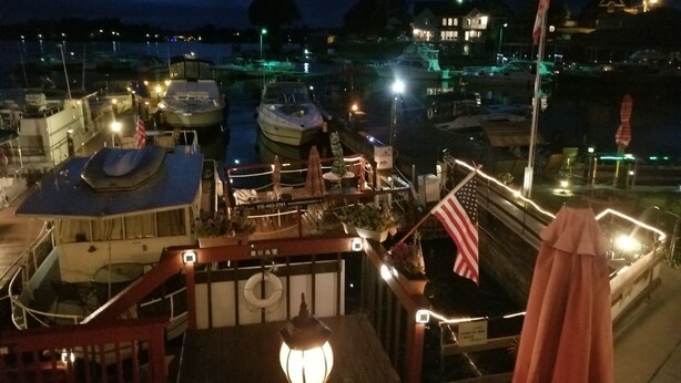 Un port de plaisance de nuit, avec des bateaux amarrés, un drapeau et un bâtiment portant une enseigne.