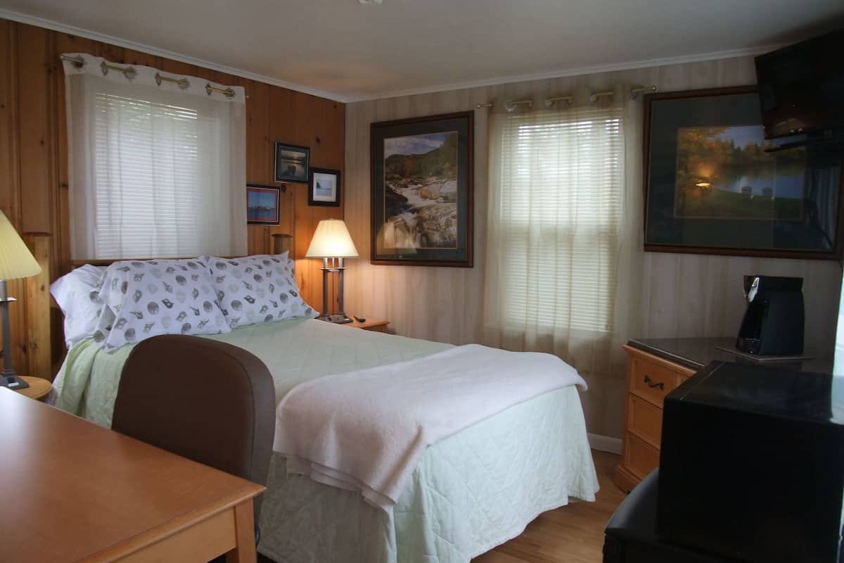 Een hotelkamer met een bed, nachtkastje, lamp en een schilderij aan de muur.