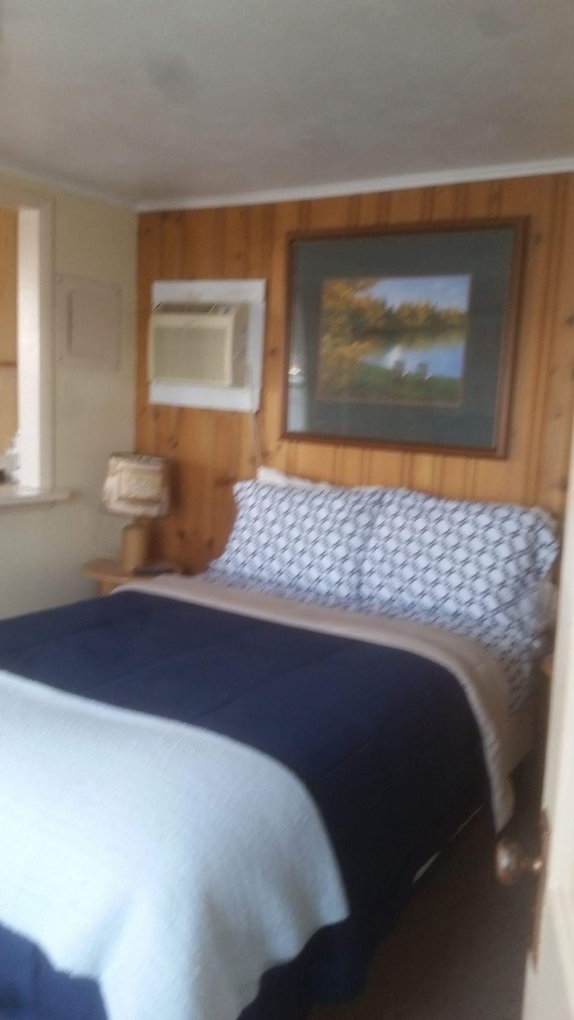 Un dormitorio con cama, ventana, cuadro y lámpara.