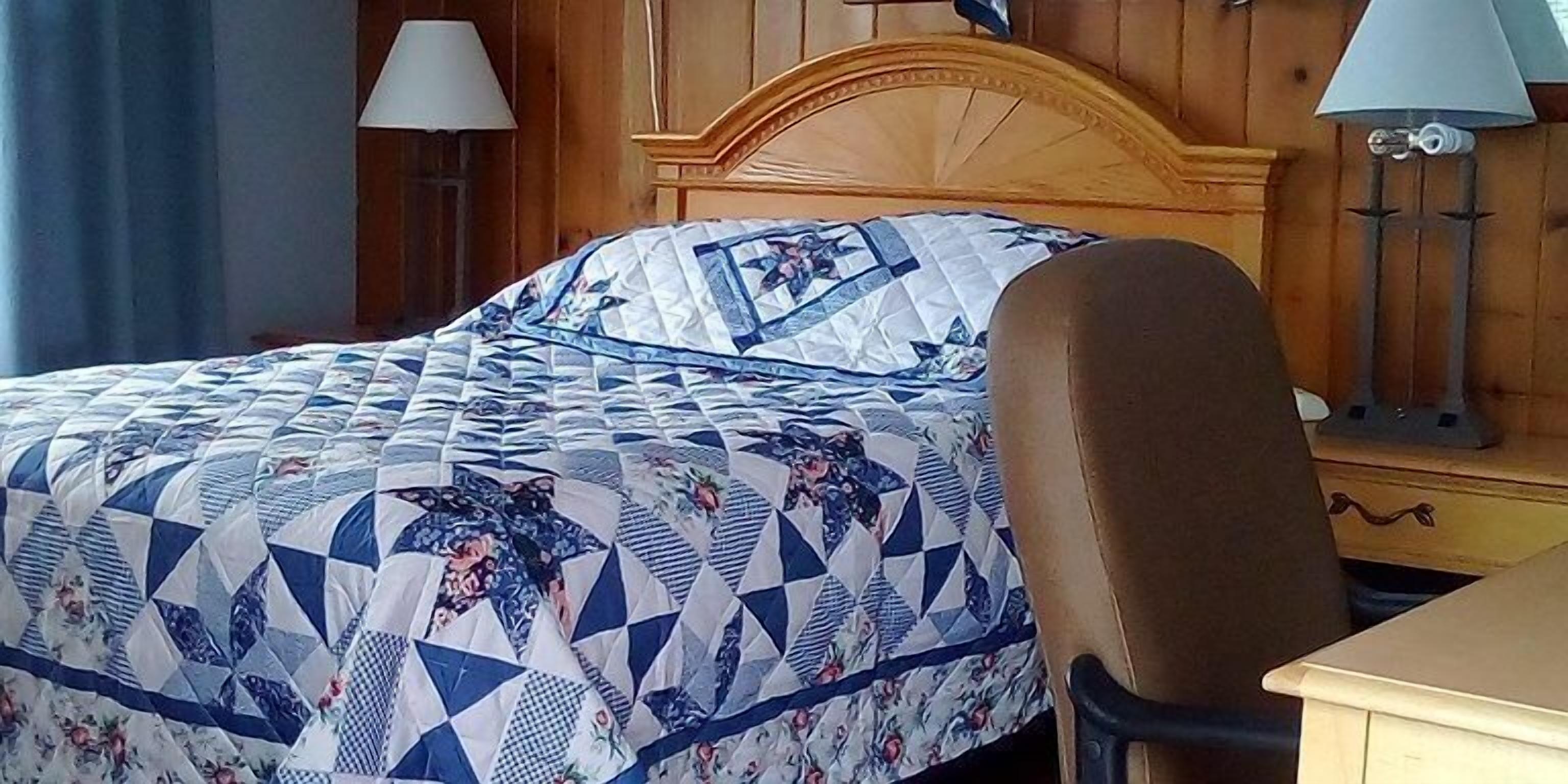 A neatly made bed with a patterned quilt, a wooden headboard, and a nightstand with a lamp.