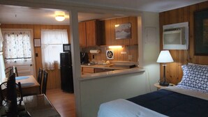 Une chambre d’hôtel de taille réduite, équipée d’une kitchenette, d’un lit, d’un bureau et d’une chaise.