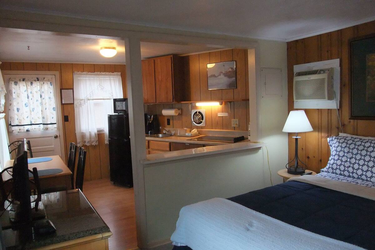 Een kleine hotelkamer met een kitchenette, een bed, een bureau en een stoel.