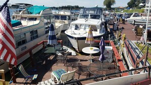 Un port de plaisance où plusieurs bateaux sont amarrés, avec des tables et des chaises à l’extérieur, protégées par des parasols, et un drapeau.