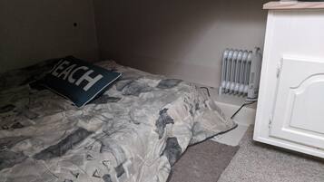 A bedroom with a bed, a pillow with 'SEACH' text, a radiator, and a white cabinet.