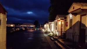 Une rangée de bâtiments d’un seul étage, dotés de garages attenants, d’un espace de stationnement couvert et d’une rue bien éclairée la nuit.