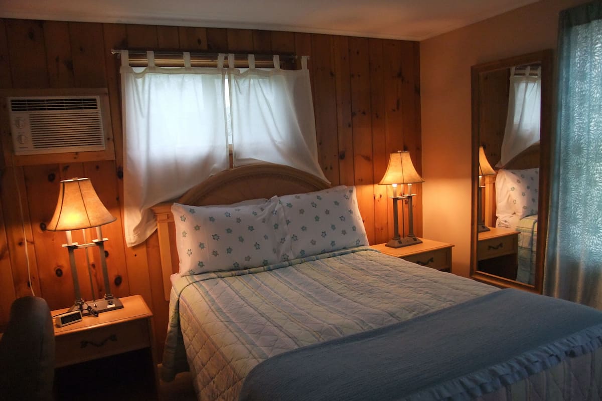 Een slaapkamer met een bed, twee bedlampen, een spiegel en een raam met gordijnen.