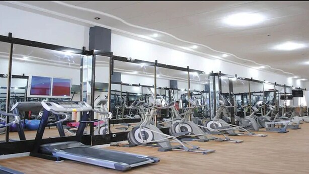 A gym with multiple exercise machines, mirrors, and a wooden floor.