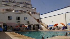 A pool area with a staircase leading to a building, outdoor seating with umbrellas, and a clear sky.