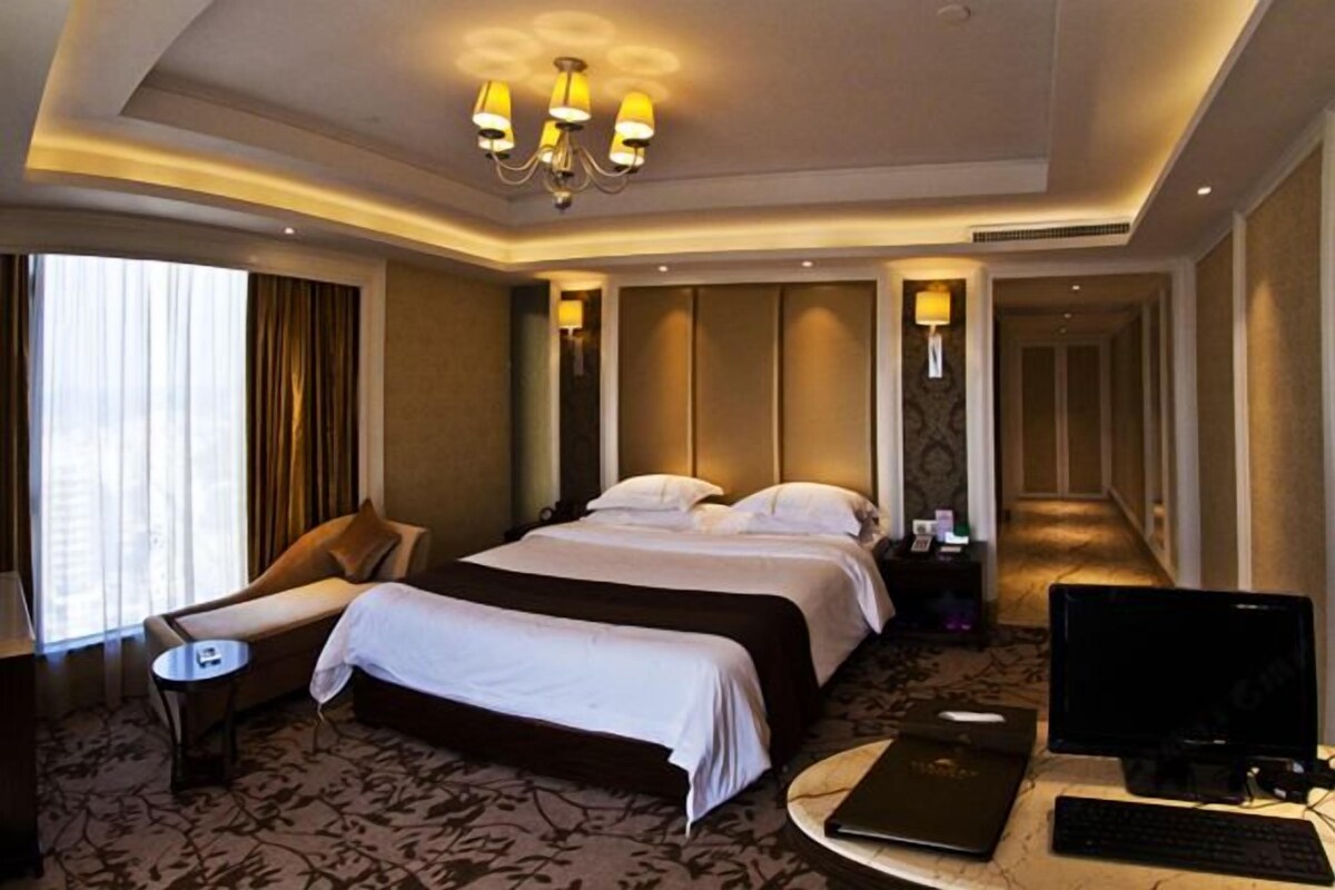 A hotel room with a king-sized bed, a desk with a computer, a chair, and a television.
