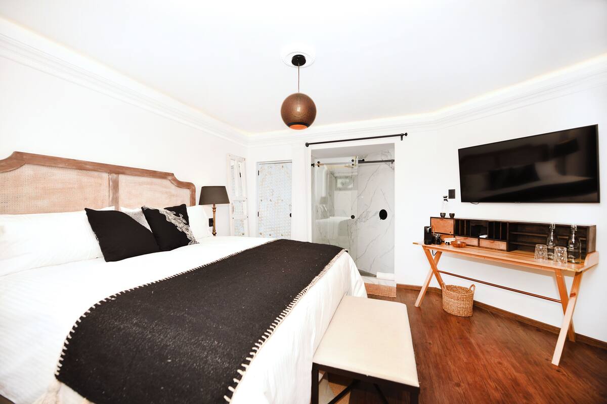 Quarto com cama, mesa de cabeceira, televisão e área de chuveiro.