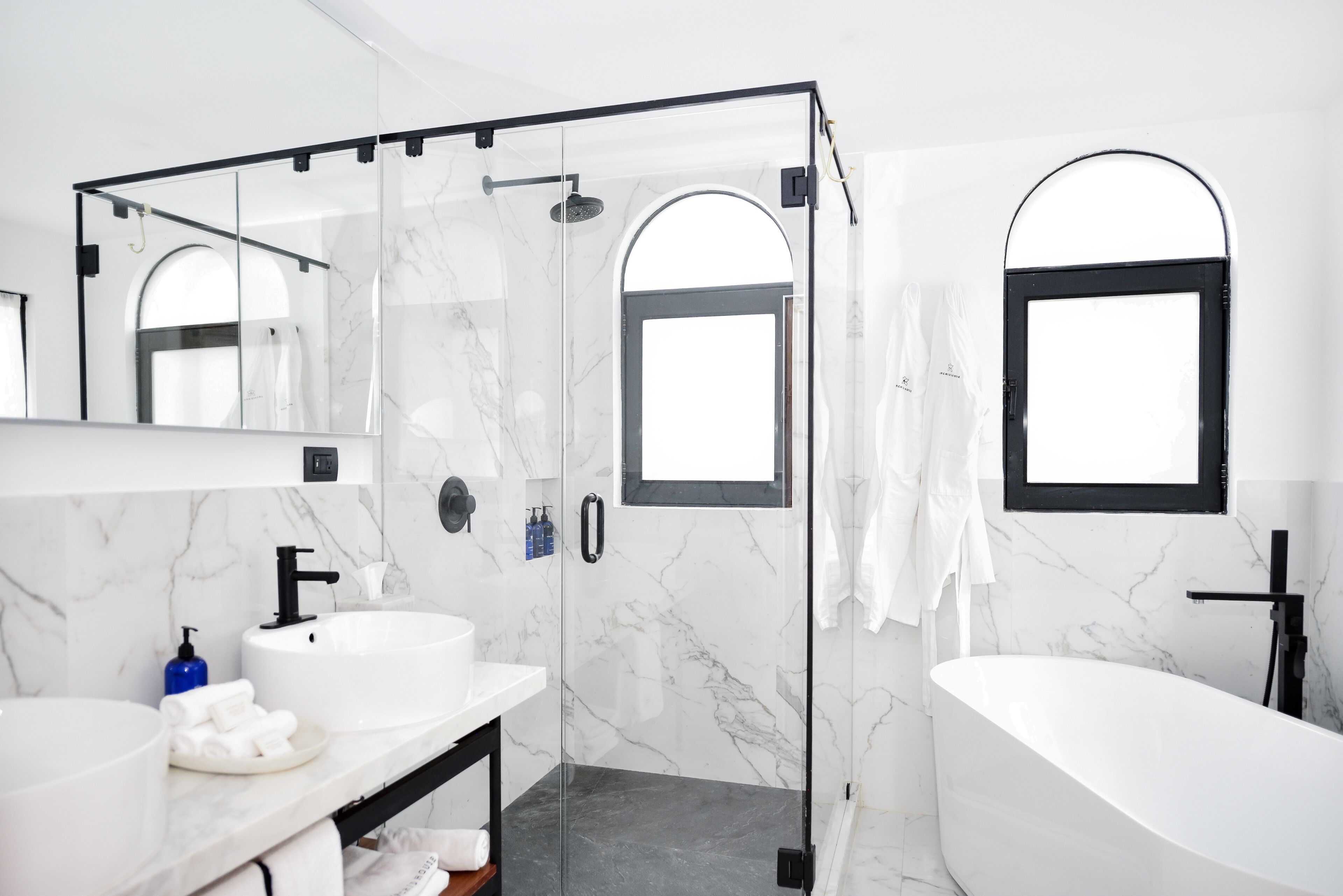 Un baño moderno con ducha envuelta en vidrio, una bañera independiente y un espejo grande sobre el lavamanos.