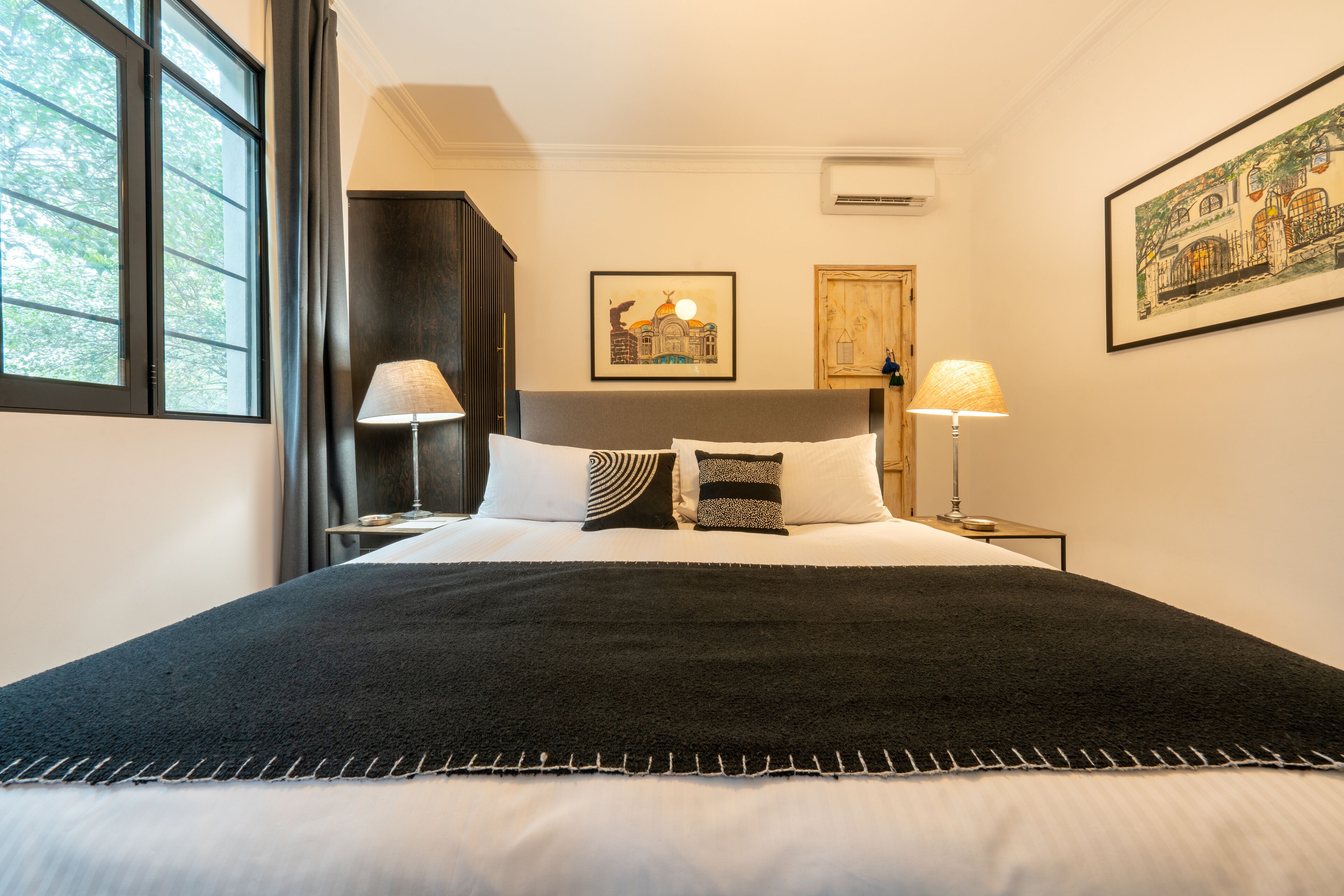 A hotel room with a large bed, two bedside lamps, a framed picture on the wall, and a window with curtains.