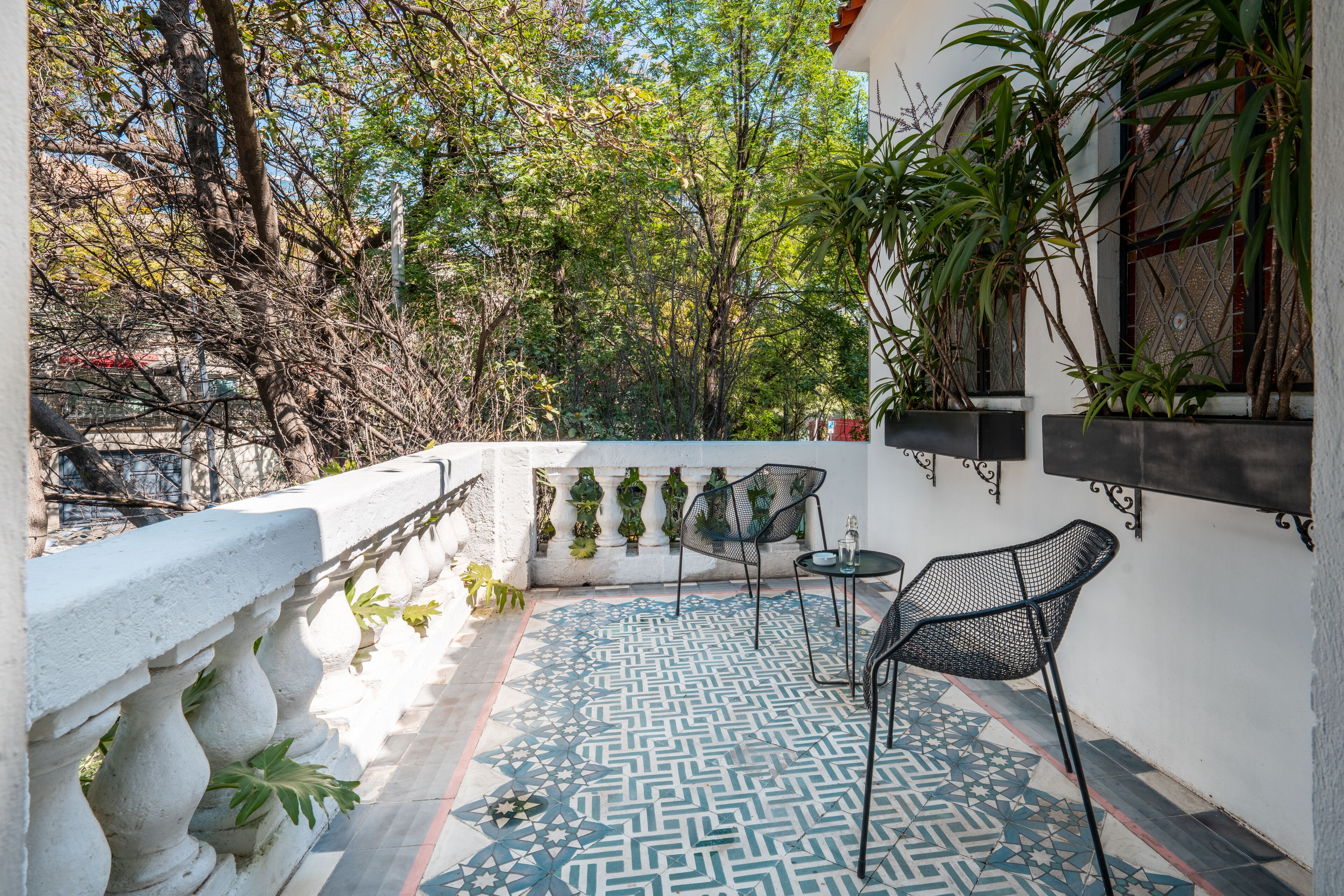 Un balcon avec des carreaux de sol à motifs, deux chaises en métal, une petite table et des plantes en pot.
