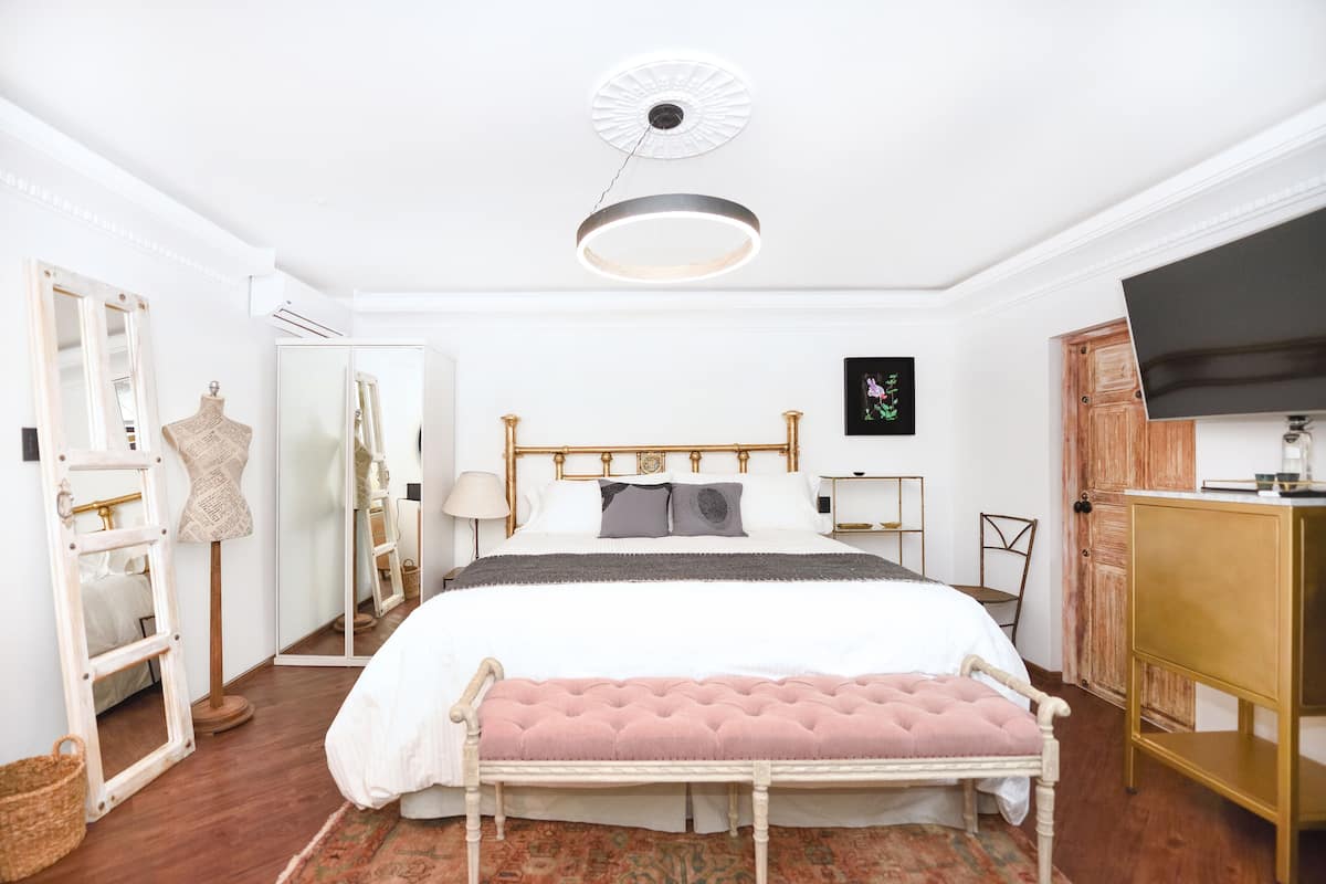 Quarto com cama, mesas de cabeceira, espelho, guarda-roupa e televisão.
