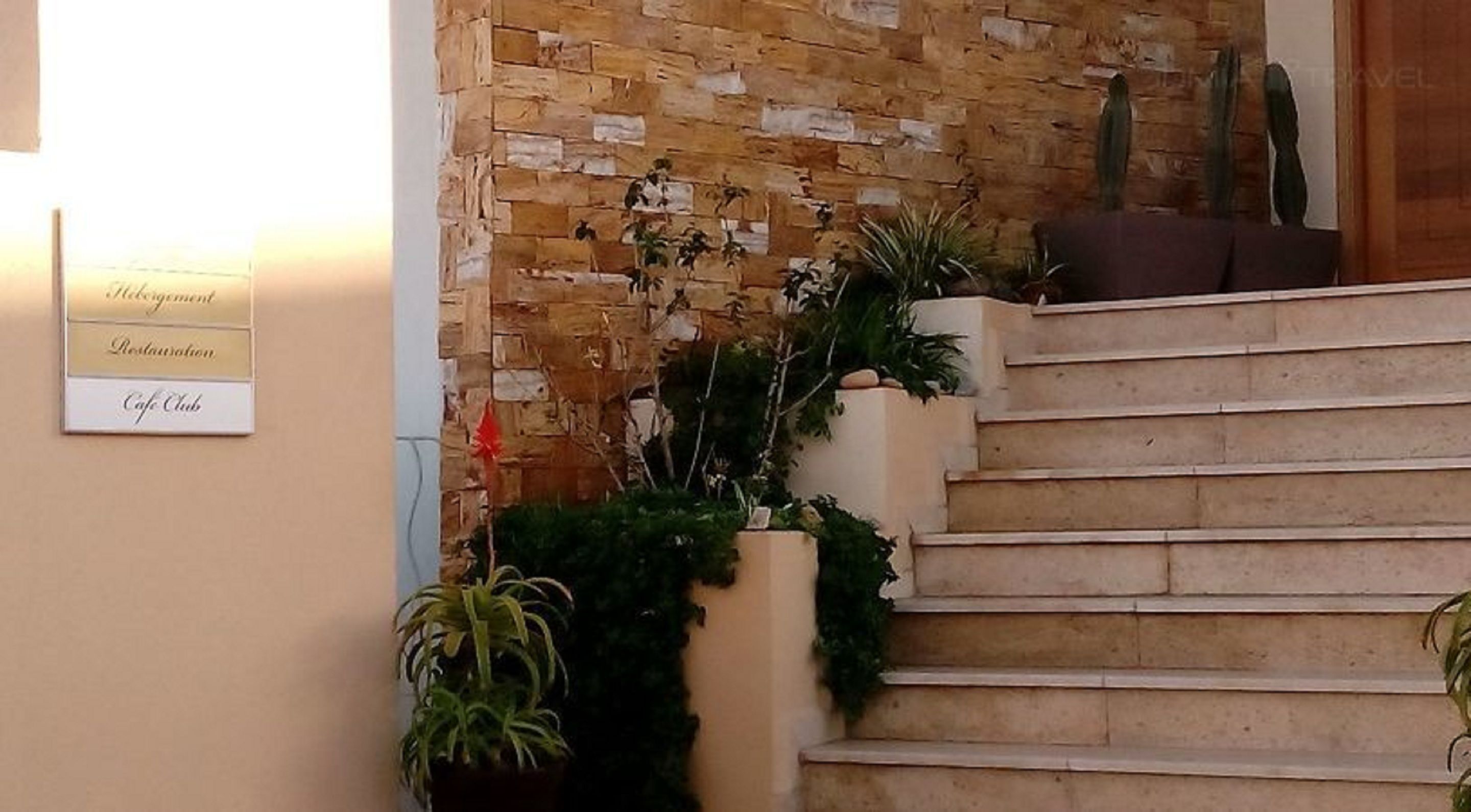 A staircase with a stone wall backdrop, potted plants, and a sign indicating amenities like a cafe and restaurant.