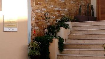 A staircase with a stone wall backdrop, potted plants, and a sign indicating amenities like a cafe and restaurant.