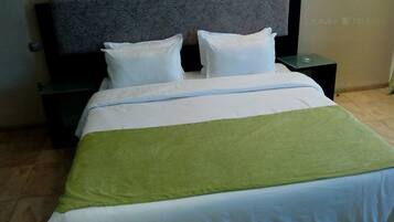 A neatly made bed with white bedding and a green throw blanket, two white pillows, and a dark headboard.