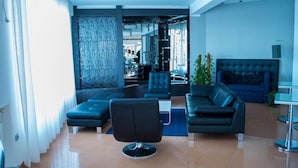 Una sala moderna con un sofá negro, un sillón negro y una pared azul decorativa.