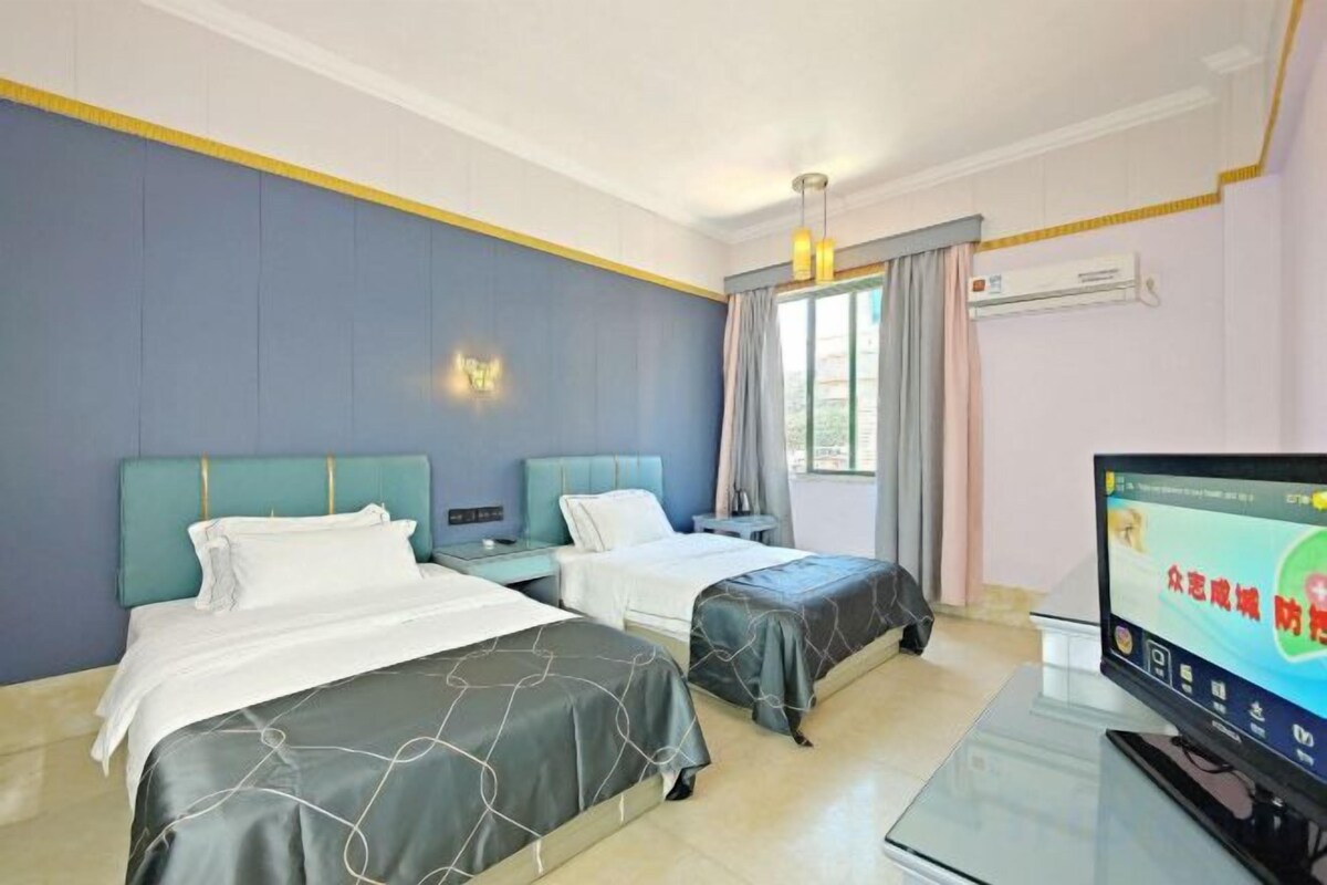 A hotel room with two beds, a television, and a window with curtains.