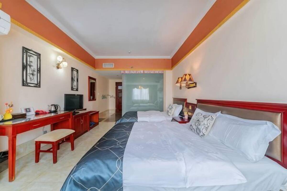 Habitación de hotel con cama, escritorio, televisión y vista al pasillo.