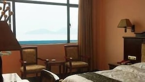 Une chambre d’hôtel avec un lit, un bureau, deux chaises, une lampe et une vue sur la mer.