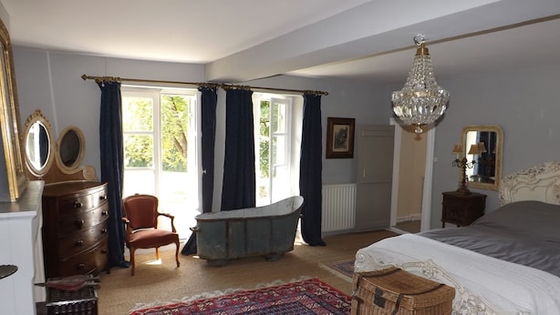 A bedroom with a large bed, a chandelier, a bathtub, and a red patterned rug. - Domaine de Lalat (Montemboeuf)