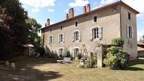 A two-story building with multiple windows and shutters, surrounded by a grassy yard and some trees. - Domaine de Lalat (Montemboeuf)