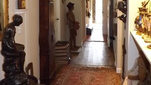 A narrow hallway with a wooden floor, a patterned rug, a large mirror, and a statue. - Domaine de Lalat (Montemboeuf)
