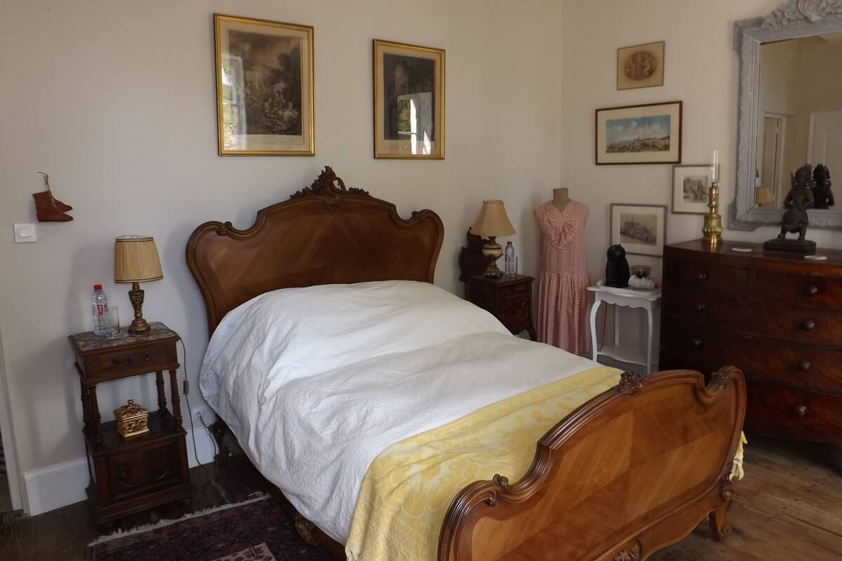 Een slaapkamer met een houten bed, nachtkastjes, een dressoir en ingelijste foto’s aan de muur.