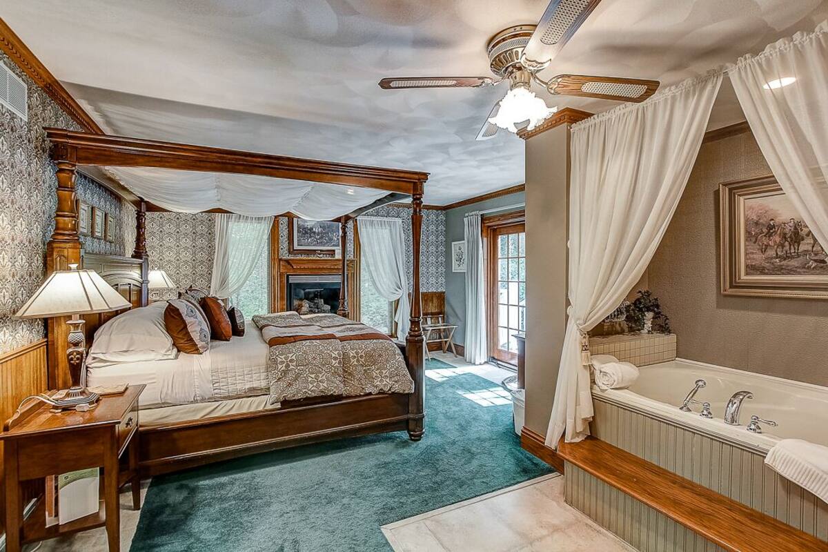 A four-poster bed with a canopy, a large bathtub, and a ceiling fan.