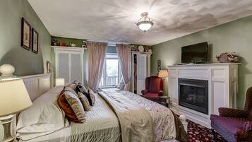 A bedroom with a bed, a television, a fireplace, and a window with curtains.