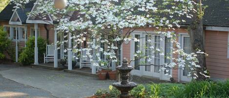A traditional house with a front porch, a fountain, and blooming trees.
