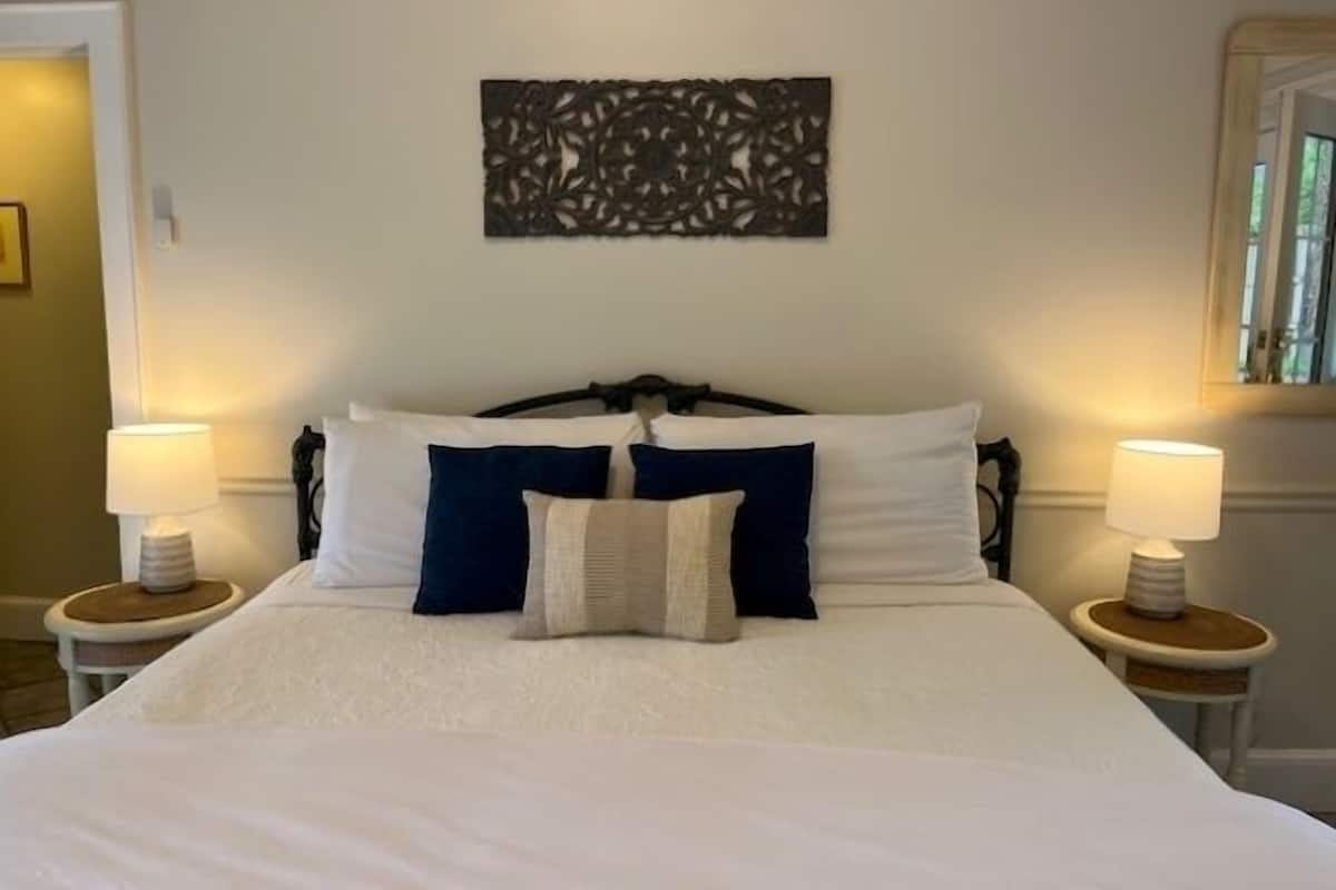 A neatly made bed with white and navy blue bedding, two bedside lamps, and a decorative wall piece above the bed.