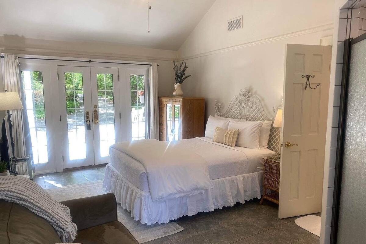 A bedroom with a large bed, a sofa, a dresser, and a door leading to a balcony.