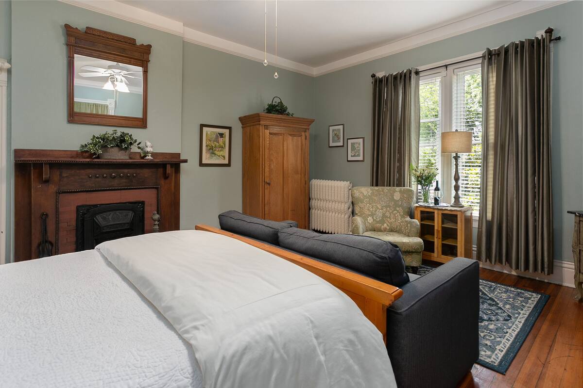 A bedroom with a bed, a wooden cabinet, a chair, and a fireplace.