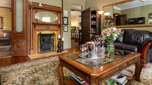 A living room with a fireplace, a leather sofa, a coffee table with decorative items, and a large mirror. - Beaufort House Inn (Asheville)