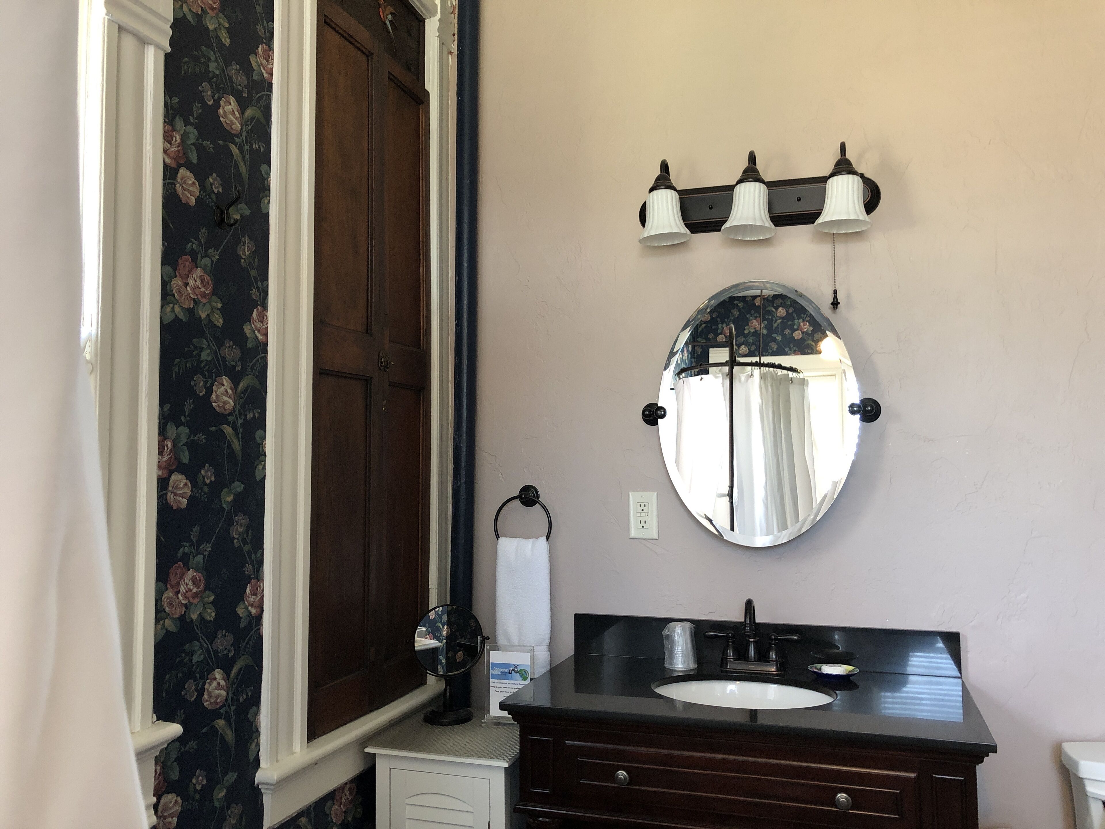 A bathroom with a dark wooden vanity, a round mirror, and a wall-mounted light fixture.