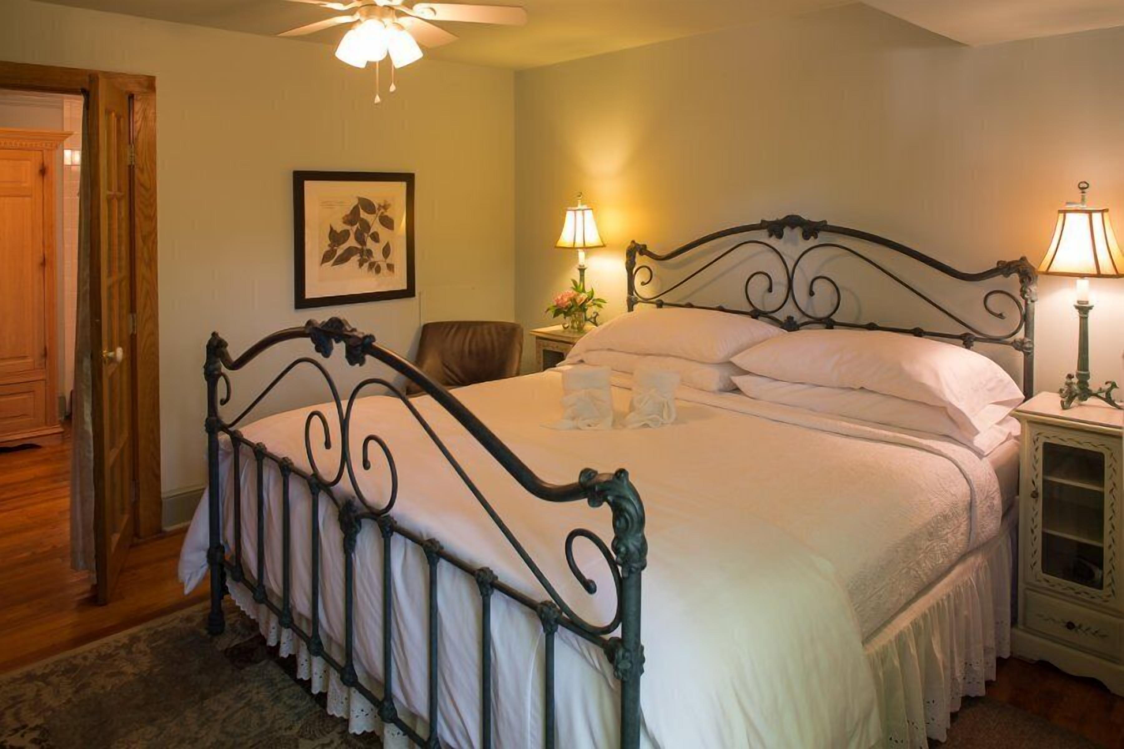 A neatly made bed with a metal frame, two bedside lamps, a framed picture on the wall, and a wooden door.