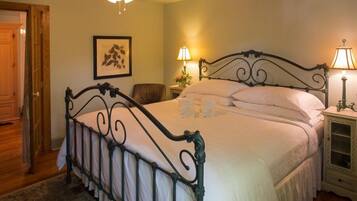 A neatly made bed with a metal frame, two bedside lamps, a framed picture on the wall, and a wooden door.