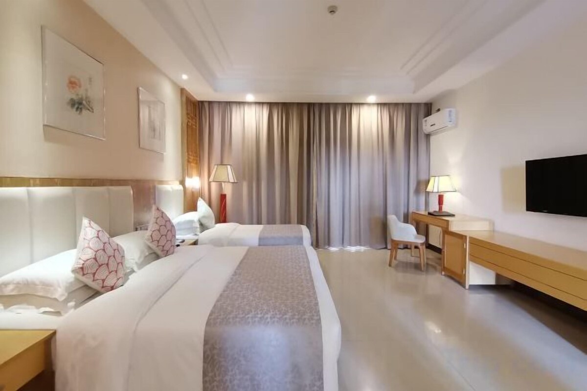 A hotel room with two beds, a desk, a chair, a TV, and a window with curtains.
